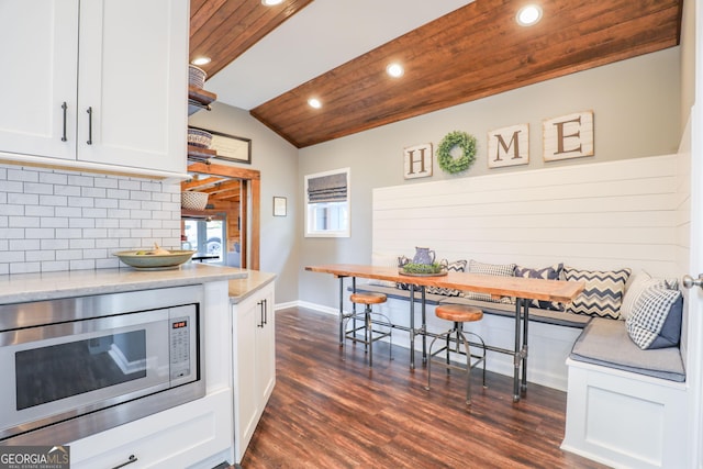 kitchen featuring dark wood finished floors, breakfast area, stainless steel microwave, wood ceiling, and white cabinets