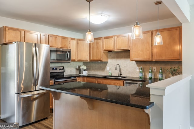 kitchen featuring tasteful backsplash, appliances with stainless steel finishes, dark stone countertops, a peninsula, and a sink