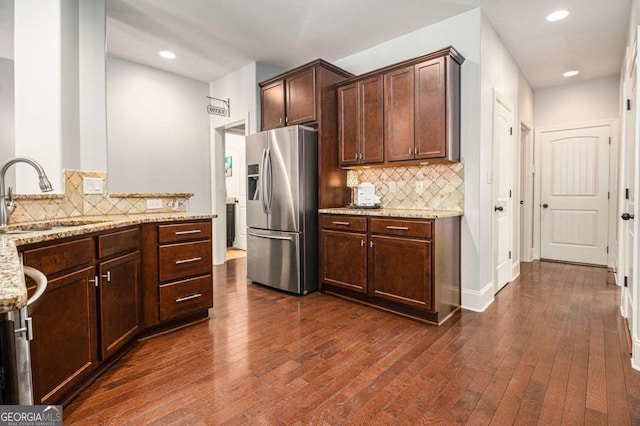 kitchen featuring tasteful backsplash, dark wood-style flooring, light stone countertops, stainless steel refrigerator with ice dispenser, and a sink