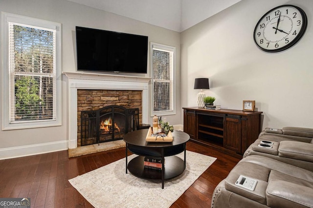 living area with dark wood-style flooring, a stone fireplace, and baseboards