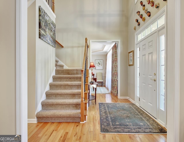 foyer entrance with stairs, baseboards, a high ceiling, and wood finished floors