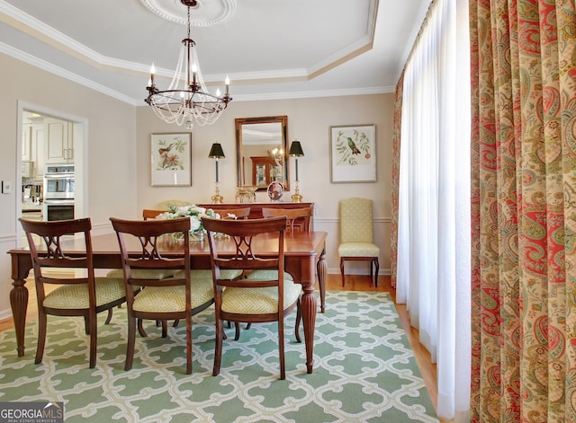 dining space featuring light wood-style floors, a raised ceiling, crown molding, and an inviting chandelier