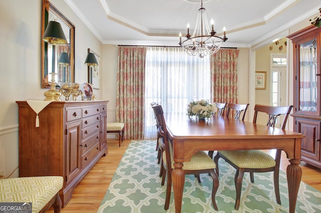 dining area featuring light wood-style floors, ornamental molding, and a raised ceiling