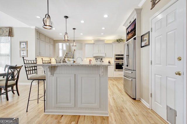 kitchen featuring light wood-style flooring, light stone counters, a breakfast bar, stainless steel appliances, and backsplash