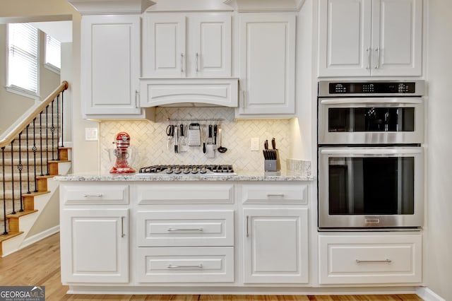 kitchen featuring stainless steel appliances, light stone counters, white cabinetry, and tasteful backsplash