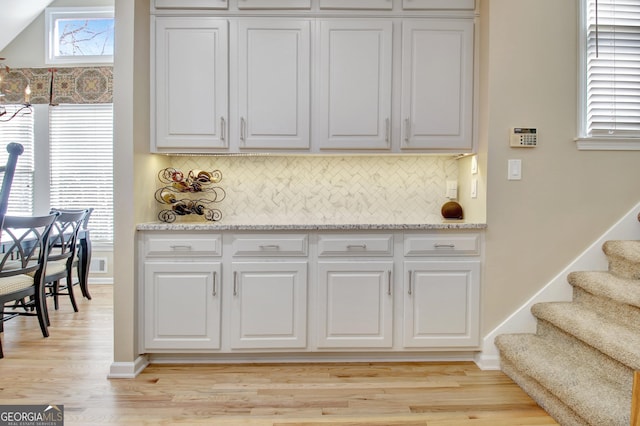 kitchen featuring light stone counters, visible vents, white cabinetry, backsplash, and light wood finished floors