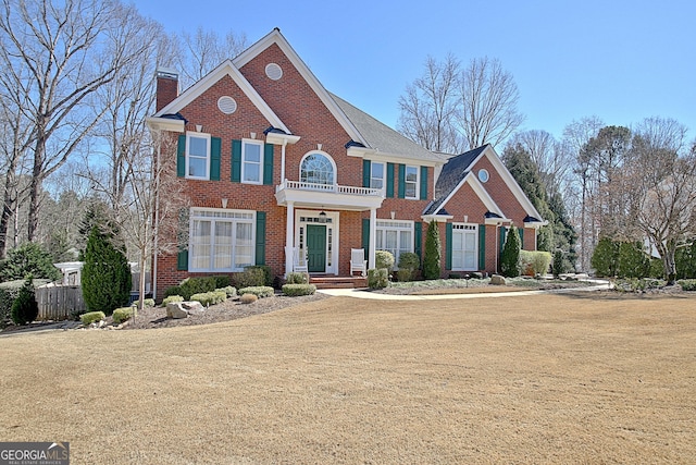 view of front of property featuring a front yard, brick siding, a chimney, and a balcony