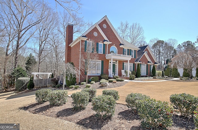 view of front of property featuring a chimney, brick siding, and a balcony