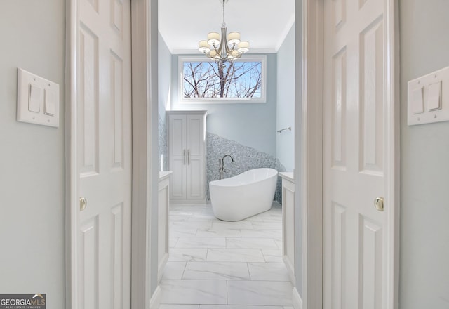 full bath featuring a notable chandelier, a freestanding bath, marble finish floor, ornamental molding, and a closet