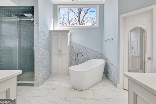 bathroom featuring wainscoting, marble finish floor, a freestanding tub, a shower stall, and tile walls