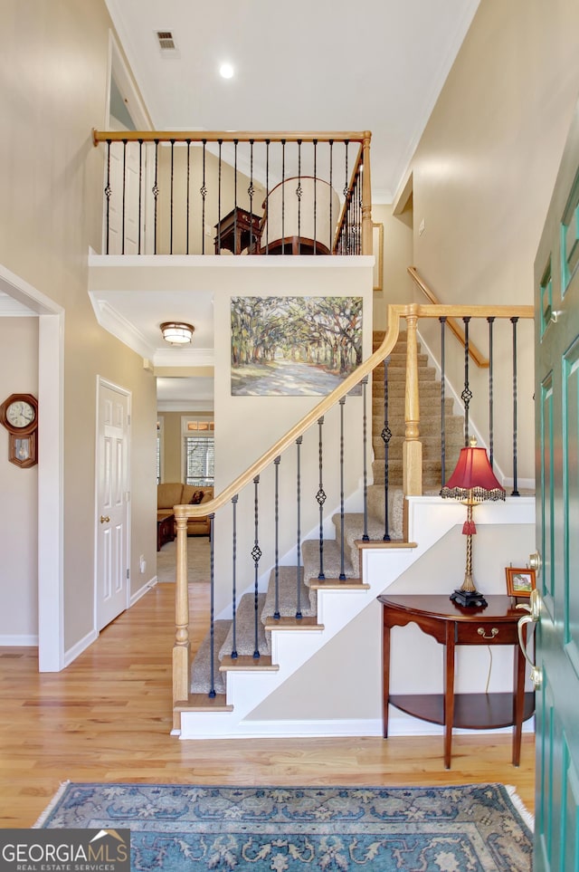 stairway with crown molding, a towering ceiling, baseboards, and wood finished floors