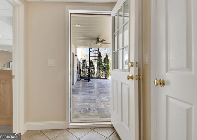 doorway with light tile patterned flooring, ceiling fan, and baseboards