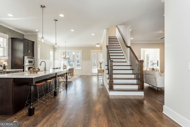 kitchen featuring a kitchen island with sink, a breakfast bar, a sink, ornamental molding, and dark wood finished floors