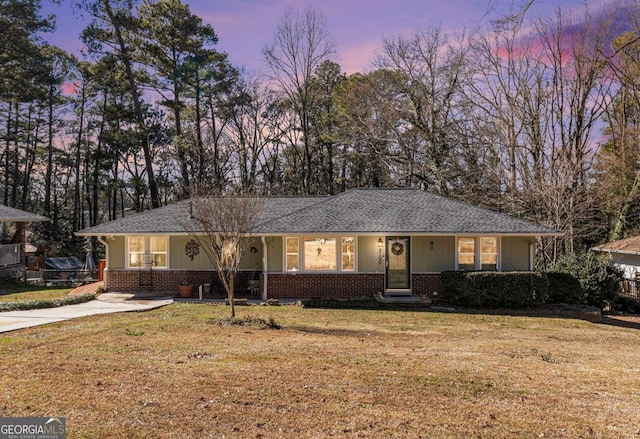 ranch-style home featuring a shingled roof, a front yard, brick siding, and driveway