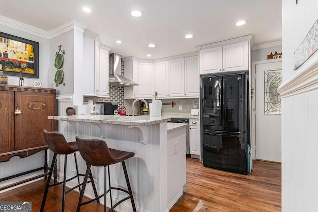 kitchen featuring white cabinets, wall chimney exhaust hood, freestanding refrigerator, a peninsula, and crown molding