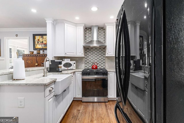 kitchen featuring a peninsula, a sink, wall chimney range hood, black fridge, and gas range