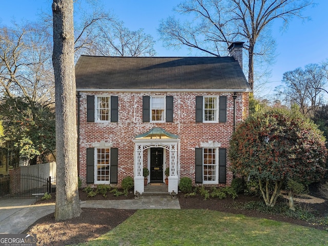 view of front facade with brick siding, fence, a chimney, and a front lawn