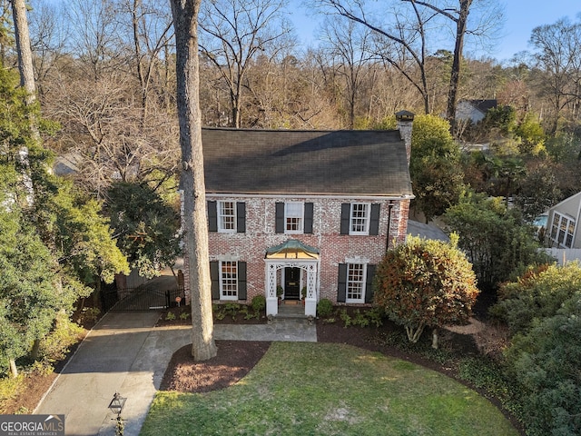 view of front of home with a front yard, a gate, a chimney, and brick siding