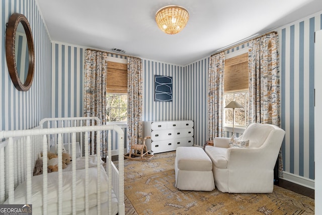 bedroom with visible vents, a crib, baseboards, and wallpapered walls