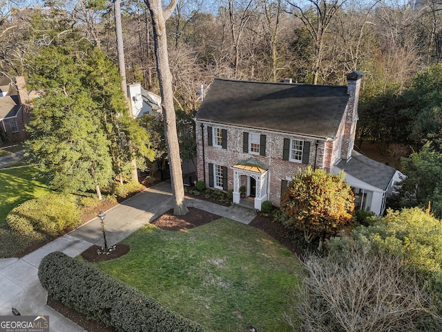 colonial-style house with a chimney, a front lawn, and brick siding