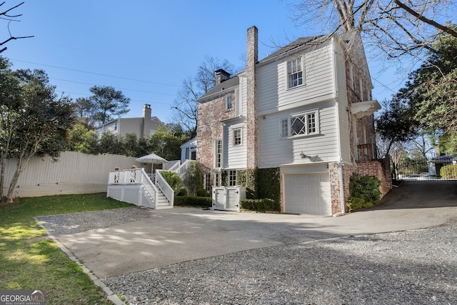 exterior space featuring a garage, brick siding, fence, stairs, and a chimney