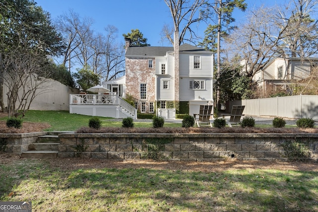 back of property featuring a deck, a chimney, fence, and a lawn