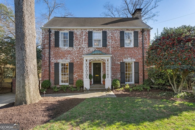 colonial house featuring brick siding, a chimney, and a front lawn