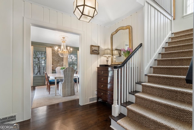 staircase featuring wood finished floors, visible vents, and a notable chandelier