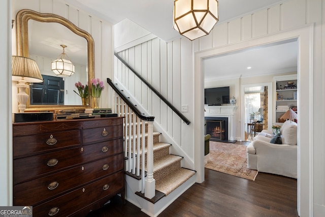 stairs featuring a lit fireplace, crown molding, and wood finished floors