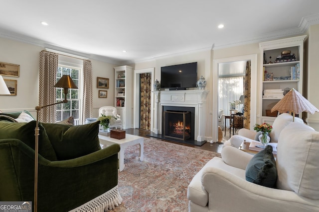 living room featuring built in shelves, crown molding, recessed lighting, wood finished floors, and a lit fireplace