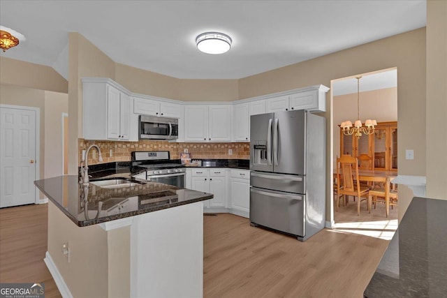 kitchen featuring white cabinets, appliances with stainless steel finishes, a peninsula, light wood-type flooring, and a sink