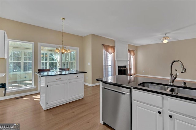 kitchen featuring a fireplace, a sink, white cabinetry, stainless steel dishwasher, and dark countertops