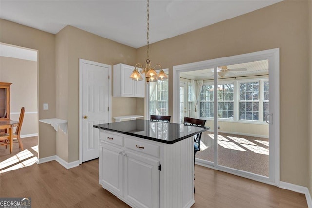 kitchen with dark countertops, light wood-style floors, white cabinetry, and hanging light fixtures