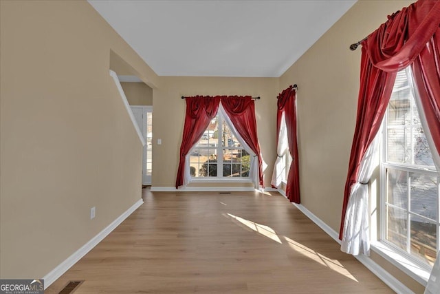 empty room featuring wood finished floors, visible vents, and baseboards