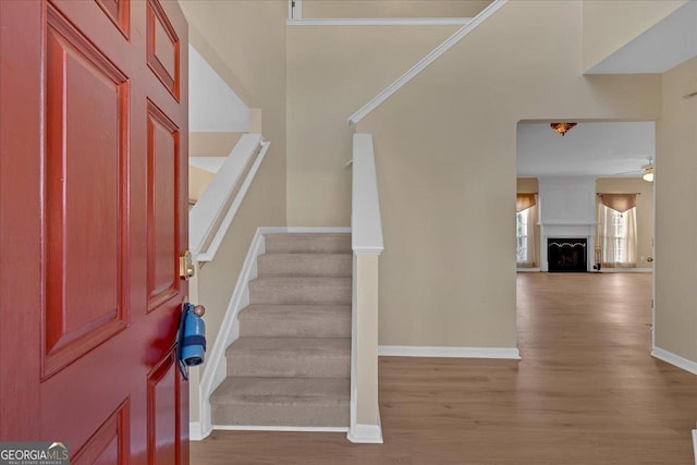 entryway with a fireplace with raised hearth, wood finished floors, stairs, and baseboards