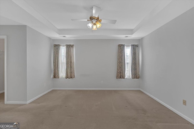 carpeted spare room featuring baseboards, visible vents, a tray ceiling, and a ceiling fan