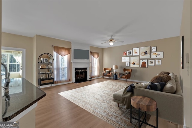 living area featuring a fireplace with flush hearth, a healthy amount of sunlight, ceiling fan, and light wood finished floors