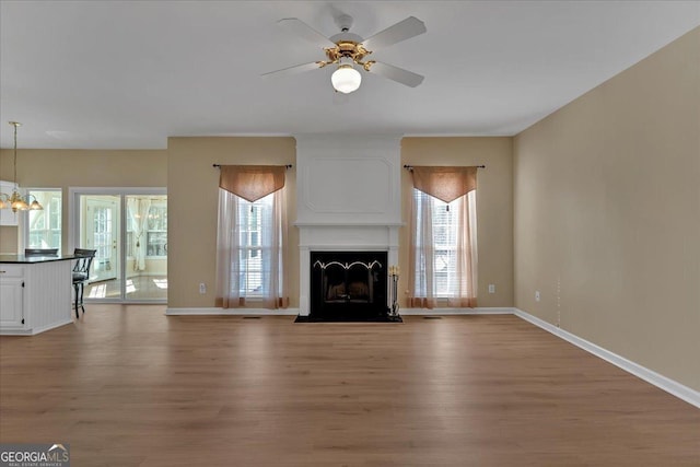 unfurnished living room featuring a fireplace with flush hearth, baseboards, and wood finished floors