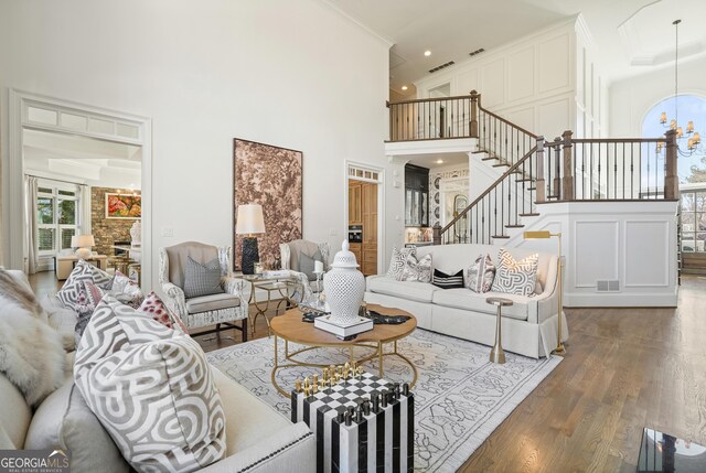 living room featuring a notable chandelier, visible vents, a high ceiling, wood finished floors, and stairs