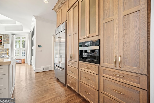 kitchen with built in fridge, crown molding, visible vents, light wood-style flooring, and baseboards