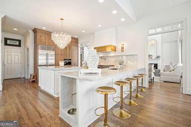 kitchen featuring stainless steel built in refrigerator, premium range hood, a peninsula, and wood finished floors