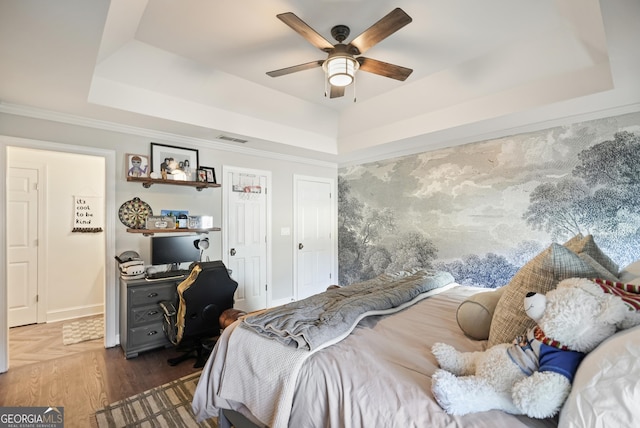 bedroom with a tray ceiling, wood finished floors, and visible vents