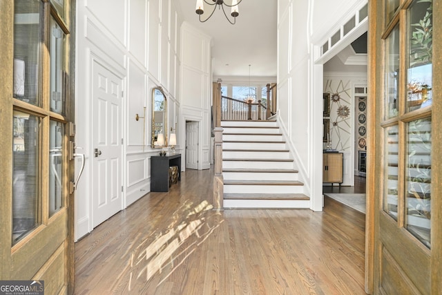 entryway featuring a notable chandelier, stairway, wood finished floors, and a decorative wall