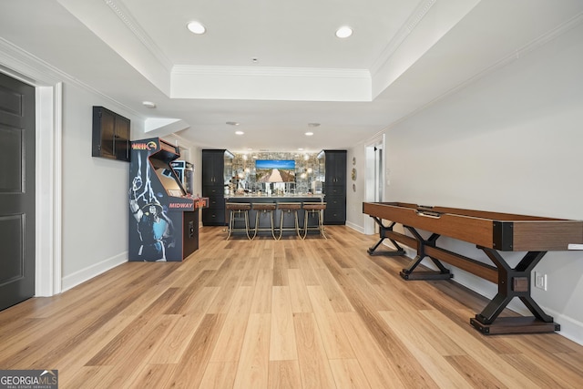 interior space with ornamental molding, a bar, a raised ceiling, and light wood-style flooring