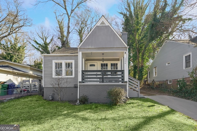 view of front facade with covered porch, a front lawn, and a chimney