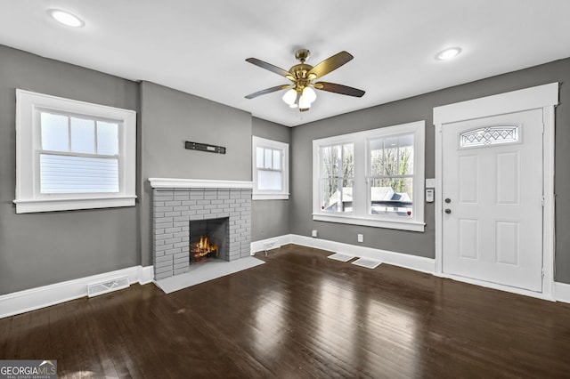 unfurnished living room with a brick fireplace, visible vents, baseboards, and wood finished floors