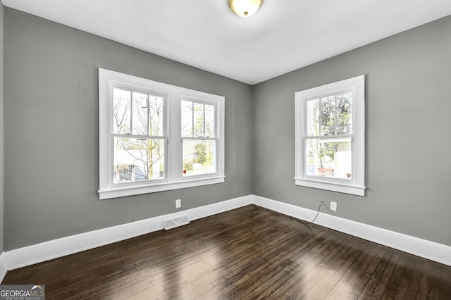 unfurnished room featuring dark wood-style floors, visible vents, and baseboards