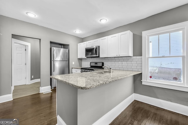 kitchen featuring dark wood-style floors, appliances with stainless steel finishes, a peninsula, light stone countertops, and a sink