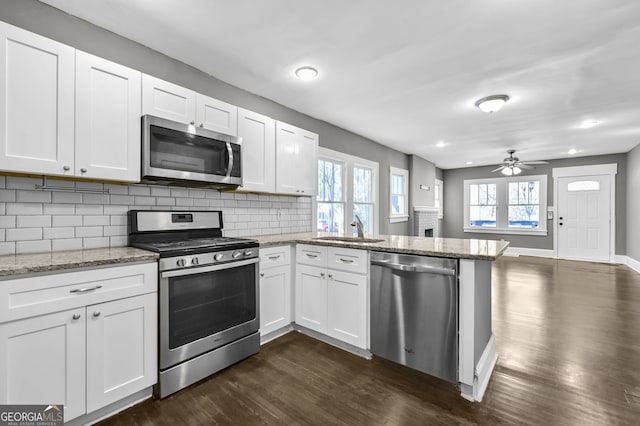 kitchen with tasteful backsplash, appliances with stainless steel finishes, white cabinets, a sink, and a peninsula