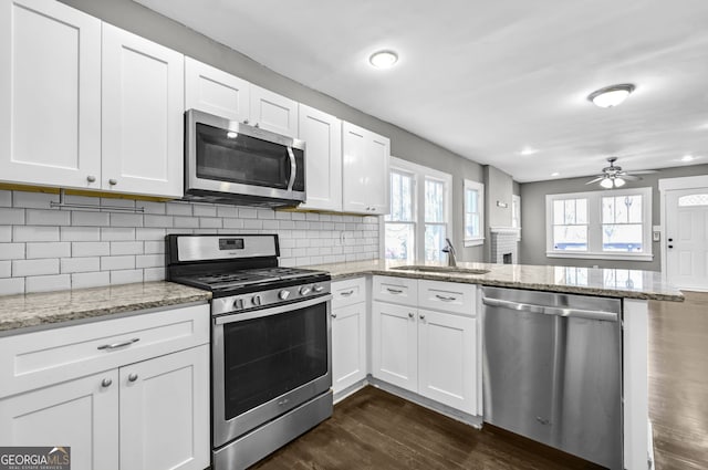 kitchen featuring stainless steel appliances, a peninsula, a sink, and white cabinetry